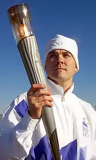 Photographie d'un homme en bonnet et survêtement blanc, portant une torche allumée dans la main droite.