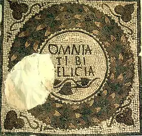 Pavement montrant la phrase « Omnia tibi felicia » au milieu d'une guirlande de feuilles.