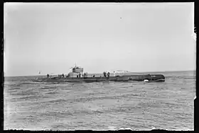 Photo noir et blanc d'un sous-marin sur une mer calme, portant l'inscription « K XII » à la proue, avec une grosse vingtaine d'hommes sur le pont et le kiosque.