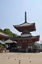 Bâtiment en bois à un étage en forme de pagode avec une base carrée et un plancher supérieure rond, murs blancs et poutres rouges.