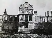 Photographie en noir et blanc d'un bâtiment de style classique très endommagé, dont il ne reste que la façade.