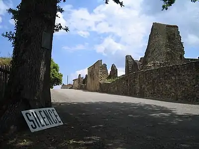 Photographie en couleurs de l'entrée du village. En bas à gauche de l'image, un panneau appelant au silence