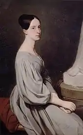 Huile sur toile représentant Marie assise de profil, elle porte une longue robe gris pâle assez ample et a les mains jointes. Son regard est songeur.