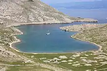 Une anse maritime presque fermée, un voilier au mouillage au milieu.