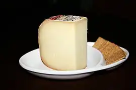 Vue d’une assiette blanche contenant une tranche de tomme de fromage et des biscuits rectangulaires.
