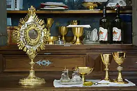 Au centre, deux burettes en verre, parmi des objets liturgiques.