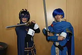 Photographie de deux personnes costumées, portant des perruques bleues. L'une porte un masque et les deux portent des épées.