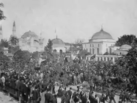 photographie noir et blanc : une foule dans la rue devant des bâtiments à dôme et minarets