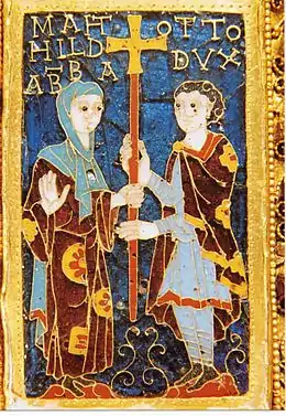 Deux personnages tiennent une croix : une femme avec une robe bordeaux et jaune avec un voile bleu clair, et un homme en tunique gris bleu avec un manteau bordeaux à fleurs jaunes