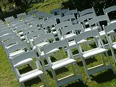 Une dizaine de rangées de chaise en plastique blanc sur une pelouse
