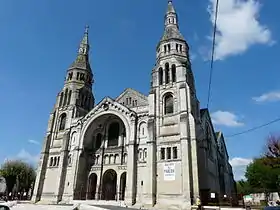 Photo représentant la façade sud ensoleillée de l'église Saint-Martin. Le portail-porche immense est encadré par deux clochers-flèches symétriques.