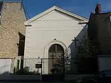 Photo représentant le temple protestant de Périgueux. Derrière une grille en fer forgé, la façade ensoleillée est percée d'un portail en bois à double vantail.