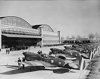 Photo noir et blanc de douze chasseurs Curtiss alignés sur un aérodrome devant un groupe d'officiels