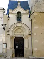Un édifice religieux étroit en tuffeau, avec un fronton sculpté et un portail néo-roman.