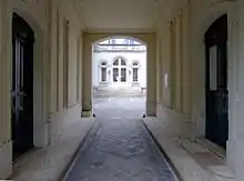 Photo en couleur d'un large passage pavé entre deux parties d'immeuble, ouvrant au fond sur une cour claire.