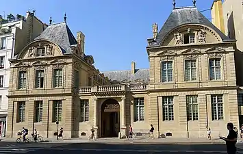 Portail cocher, dressé contre un corps bas en terrasse (disposition restituée lors de la restauration en 1950-1970) et qui donne accès à la cour pavée.