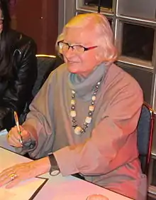 Personne âgée assise, souriante, stylo en main