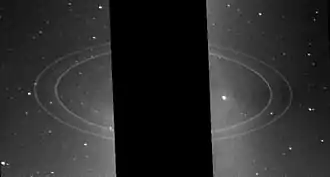 Image éloignée de la planète, trois grands anneaux sont visibles et la planète cachée par une bande noire.