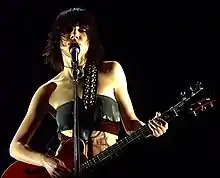 Image d'une femme brune habillée d'un haut noir jouant de la guitare et chantant dans un micro
