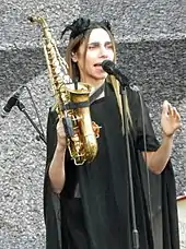 Image d'une femme habillée de noir tenant un saxophone et chantant dans un micro