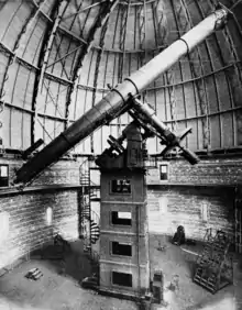 Photographie en noir et blanc d'un grand télescope sous un coupole métallique.