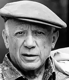 Photographie en noir et blanc de Pablo Picasso montrant un homme d’âge mûr aux cheveux courts portant une casquette inclinée vers l’oreille droite.