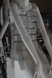 Photo d'une robe composée de tuiles de métal blanc portée par un mannequin en plastique blanc.