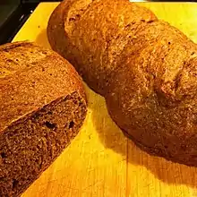 Deux pains, l'un présentant une face coupée à gauche et l'autre entier, de couleur marron sur une table en bois clair.