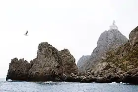 Photo de plusieurs rochers au milieu de la mer dont un surmonté par un phare