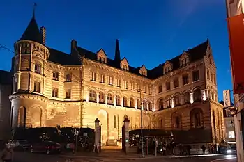  Photographie d'un imposant bâtiment médiéval, en tuffeau, éclairé la nuit. Une tour sur sa gauche