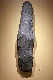 Photo d'une pierre alongée taillée sur les bords, exposée sur un présentoir dans un musée.
