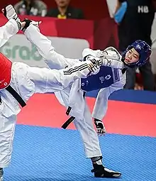 Une taekwondoïste en action portant un casque et un plastron bleu.