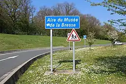 Panneau E34c d'entrée dans l'Aire du Musée de la Bresse surmontant un panneau A13a.