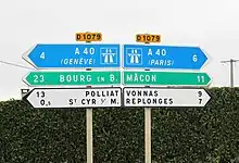 Deux panneaux indiquant la direction et le kilométrage de lieux. À gauche de haut en bas, on trouve A40 (Genève), Bourg-en-Bresse, Polliat et Saint-Cyr-sur-Menthon. À droite, on trouve A40 (Paris), Mâcon, Vonnas et Replonges.