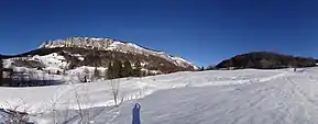 Pentes enneigées traversées par une piste de ski nordique et des montagnes en arrière-plan.