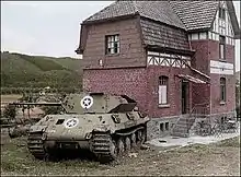 photo en couleur montrant un char de combat portant comme insigne une étoile blanche devant une maison en briques rouges.