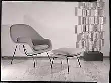 Photographie en noir et blanc d’un fauteuil et son repose-pieds sur un parquet.