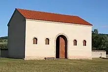 Restitution d'un bâtiment antique avec grande porte, petites fenêtres et toiture tuiles.