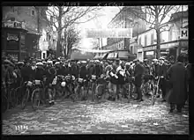 Photographie en noir et blanc de coureurs cyclistes sur une place.