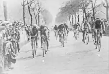 Photographie en noir et blanc d'un groupe de cyclistes au sprint à l'arrivée d'une étape.