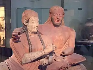 Sculpture en terre d'un couple vu à hauteur de buste, l'homme pose son bras autour des épaules de sa compagne.