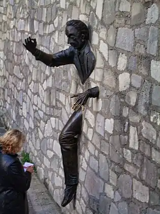 La sculpture de Jean Marais émerge du mur situé au fond de la place.