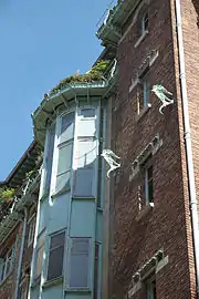 Photo en couleur et en contre-plongée d'une façade en brique avec une sorte de demi-tour en métal avec ouvertures rectangulaires en escalier