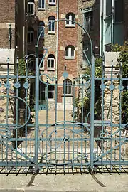 Photo en couleur d'une cour étroite entre des façades d'immeuble disparates, derrière une grille de fer forgé à arabesques