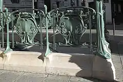 Photo en couleur et en gros plan d'une partie de balustrade comportant deux fois un socle de pierre claire et des éléments de fonte ouvragés