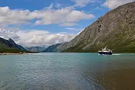 Petit bateau sur un grand lac turquoise cerné de montagnes.