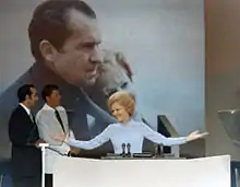 Pat Nixon à la tribune de la convention républicaine de 1972, (deux hommes et une affiche sont au second plan).