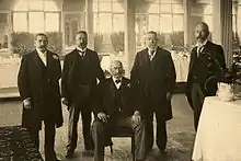 Photographie de cinq hommes en costume dans une salle de réception