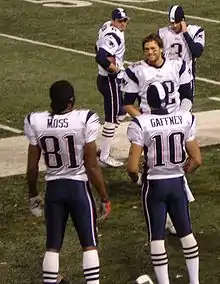 Cinq joueurs de football américains habillés de maillots blancs au bord d'un terrain de football américain.
