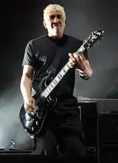 un homme en noir joue de la guitare dans une ambiance sombre.